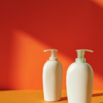 Two white pump bottles against a bold orange and yellow background, ideal for product packaging mockups.
